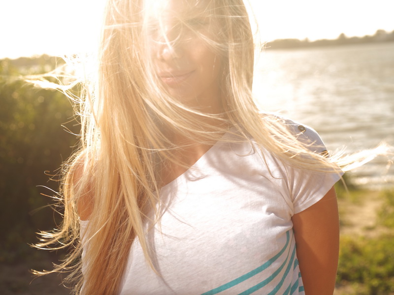 blond girl sitting near river against sun