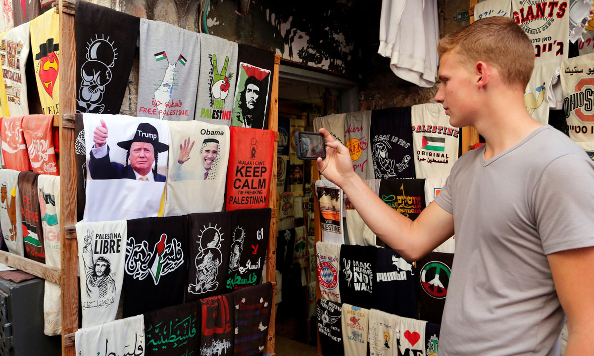 A man photographs T-shirts bearing images of newly elected U.S. President Donald Trump (L) next to one with an image of U.S President Barack Obama, displayed outside a stall in Jerusalem's Old City November 9, 2016. REUTERS/Ammar Awad