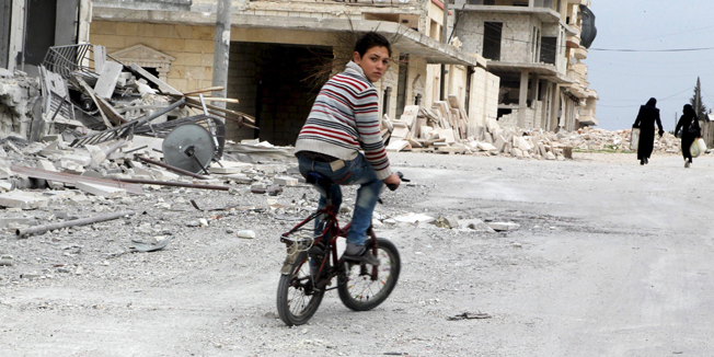 A boy rides a bicycle near damage in Kafr Hamra village, northern Aleppo countryside, Syria February 27, 2016. Picture taken February 27, 2016. REUTERS/Abdalrhman Ismail