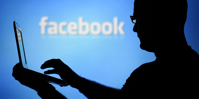 A man is silhouetted against a video screen with an Facebook logo as he poses with an Dell laptop in this photo illustration taken in the central Bosnian town of Zenica, August 14, 2013. REUTERS/Dado Ruvic (BOSNIA AND HERZEGOVINA - Tags: BUSINESS TELECOMS) - RTX12L6I