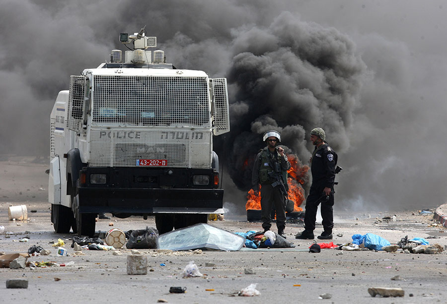Israeli police officers face Palestinians protesters marking the anniversary of Land Day in Qalandia which lies between Jerusalem and the West Bank city of Ramallah on March 30, 2012. Land Day marks the annual event that commemorates the deaths of six Arab Israeli protesters at the hands of Israeli forces during mass demonstrations in 1976 against plans to confiscate Arab land in northern Israel. AFP PHOTO/ABBAS MOMANI