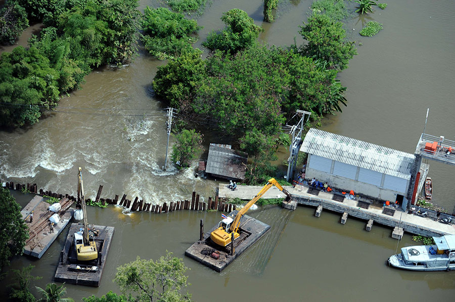 This aerial picture shows workers using mechanical diggers to reinforce a ruptured protection wall next to a flood gate in the hard-hit province of Pathum Thani, north of Bangkok, on October 16, 2011.  Flood defences protecting the Thai capital held up on October 16, but the advancing waters that have swamped the inland still threaten to engulf Bangkok in a disaster that has claimed 300 lives. Thailand's worst floods in decades have inundated huge swathes of the kingdom, swallowing homes and businesses, shutting down industry, and forcing tens of thousands of people to seek refuge in shelters.   AFP PHOTO/Christophe ARCHAMBAULT
