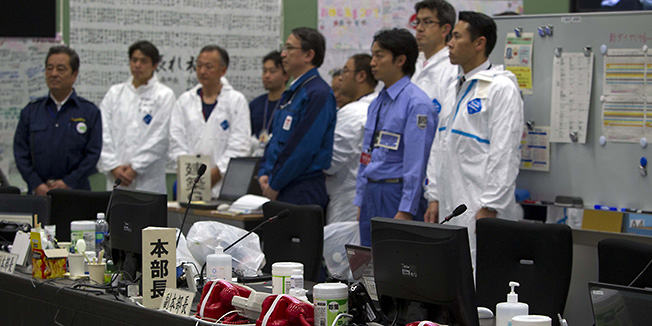 Red emergency phones sit on a desk as workers inside the emergency operation center at the crippled Fukushima Dai-ichi nuclear power station stand to listen to Japan's Minister of the Environment, Goshi Hosono, in Okuma, Japan Saturday, Nov. 12, 2011. (AP Photo/David Guttenfelder, Pool)