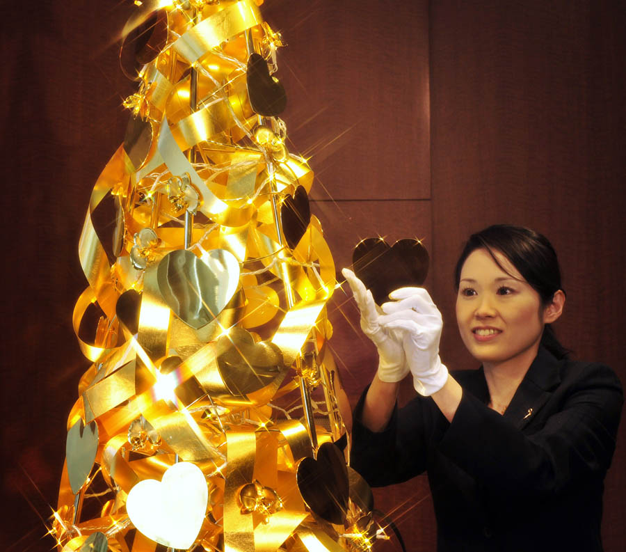 An employee of Japanese jeweller Tanaka Kikinzoku Jewelry unveils a 150 million yen (1.95 million USD) Christmas tree which will be on display till Christmas Day at the company's main shop in Tokyo on November 22, 2011. The 2.4 meter tall Christmas tree is decorated with heart and orchid shaped ornaments, ribbons and a star made of gold.  AFP PHOTO / Yoshikazu TSUNO