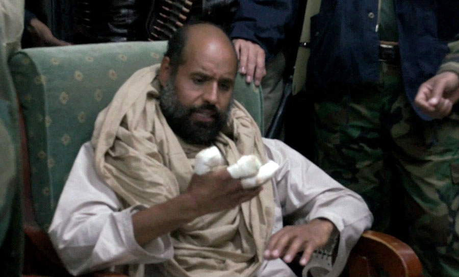 In this image taken from video made available Tuesday, Nov. 22, 2011, Moammar Gadhafi's son Seif al-Islam examines his injured hand shortly after his capture on Saturday, Nov. 19, 2011, at a safe house in the town of Zintan, Libya. The video shows Seif al-Islam arguing with his captors and admonishing them saying that Libya's regions that were united in revolution will turn against each other in the near future and rip the country apart. Seif al-Islam says his hand was injured during a recent allied bombing. (AP Photo/APTN) TV OUT