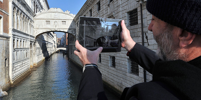 A tourist take pictures of Venice's bridge of Sighs (C-background) after it was renovated on December 1, 2011. The 'Ponte dei Sospiri' (bridge of sighs), leading from the Ducal Palace (L) to the old prison (R) had been controversially covered with advertising boards covering the scaffolding during the three years of the restoration work. AFP PHOTO / ANDREA PATTARO
