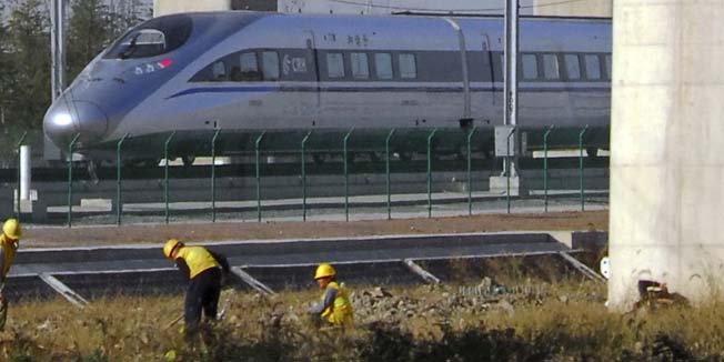 FILE - In this Dec. 3, 2010 file photo, a CRH380A high-speed passenger train runs past workers at a newly built Shanghai Hongqiao High-Speed Railway Station in Shanghai, China. China's government announced another cut in railway construction spending Friday amid concern about the debts of the world's biggest rail network and the safety of its showcase bullet trains. (AP Photo, File) CHINA OUT