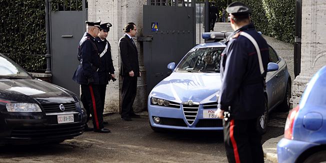Italian Carabinieri watch a police car leave the Swiss embassy in Rome on December 23, 2010. A parcel bomb exploded in the Swiss embassy in Rome today, seriously injuring the employee who opened the package, a police spokesman told AFP.  The man's hands were injured in the blast and he has been hospitalised, the spokesman said. AFP PHOTO/ FILIPPO MONTEFORTE
