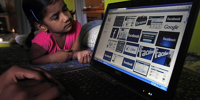 An Indian works on a laptop displaying Facebook logos as a child watches in Hyderabad, India, Friday, May 18, 2012. Facebook's stock is set to begin trading on the Nasdaq Stock Market on Friday, the day after the world's definitive online social network raised $16 billion in an initial public offering that valued the company at $104 billion. (AP Photo/Mahesh Kumar A.)