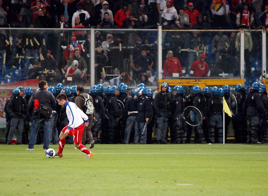 Serbia's Zoran Tosic warms up as Italian police is seen in the background confronting Serbia fans prior to the start of a Group C, Euro 2012 qualifying soccer match between Italy and Serbia, at the Luigi Ferraris stadium in Genoa, Italy, Tuesday, Oct. 12, 2010. The Italy-Serbia European Championship qualifier was called off after seven minutes of play on Tuesday after Serbia fans threw flares onto the pitch. (AP Photo/Antonio Calanni)