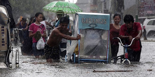 Drivers push their pedicab during a sudden downpour along floodwaters at Navotas city, north of Manila, Philippines, Wednesday, Aug. 1, 2012. Fierce winds and heavy rains from the slow-moving Typhoon Saola battered the country, displacing 154,000 people. (AP Photo/Aaron Favila)