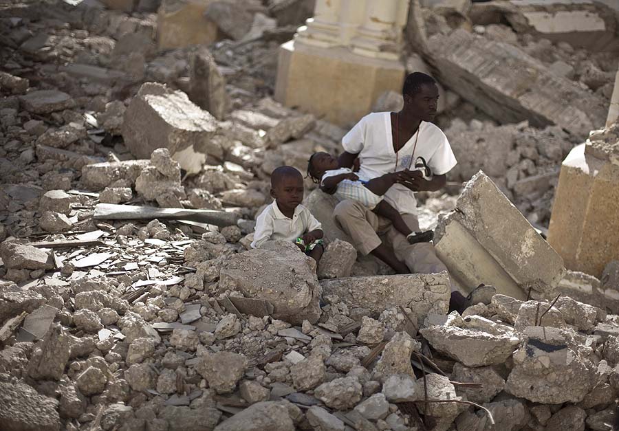 A man with two children sits in the rubble of the earthquake damaged Cathedral during a mass in Port-au-Prince, Haiti, Wednesday Jan. 12, 2011.  Wednesday marks the one year anniversary since Haiti's magnitude-7.0 earthquake that devastated the capital and is estimated to have killed more than 230,000 people and left millions homeless.  (AP Photo/Ramon Espinosa)