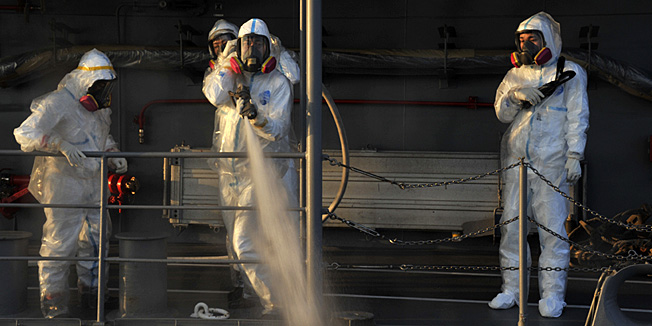 In this photo taken on Thursday, March 31, 2011 by Japan Maritime Self-Defense Force and released by Japan Defense Ministry Friday, April 1, JMSDF personnel all in protective suits spray water to clean a tugboat, not shown, that towed a U.S. military barge carrying pure water to the quay of the tsunami-stricken Fukushima Dai-ichi nuclear complex in Okumamachi, Fukushima Prefecture, northeastern Japan. (AP Photo/Japan Defense Ministry) EDITORIAL USE ONLY