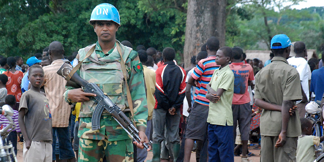 TO GO WITH AFP STORY BY PETER MARTELLA United Nations peacekeeper stands guard neaxt to a group of southern Sudanese in the village of Nzara, Western Equatoria state, near Sudans border with DR Congo on August 18, 2010. Thousands have fled their nearby villages following a series of recent attacks by guerrilla fighters believed to be Lords Resistance Army (LRA) rebels. AFP PHOTO/PETER MARTELL