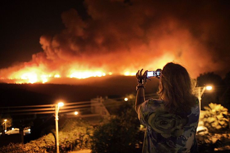 An Israeli woman holds the keys of her house in her left hand while taking a photo of a raging forest fire in the Carmel mountain from a residential house in the hills above the coastal Israeli city of Haifa, December 2, 2010. Police said at least 40 people died in the inferno, which officials said was the worst blaze in Israel's 62-year history.  TOPSHOTS  AFP PHOTO/MARCO LONGARI
