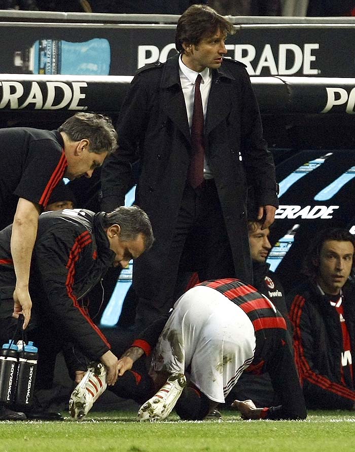AC Milan's David Beckham is assisted by a team's staff as his coach Leonardo looks on after being injured against Chievo during the Italian serie A soccer match in Milan March 14, 2010. Beckham's World Cup hopes looked to be all but over after the England midfielder went off with a suspected ruptured Achilles tendon late in AC Milan's 1-0 Serie A win over Chievo on Sunday. Beckham was getting ready to kick a ball unchallenged when he suddenly pulled up and signalled to the bench despite second-placed Milan having used all their substitutes. REUTERS/Alessandro Garofalo (ITALY - Tags: SPORT SOCCER)