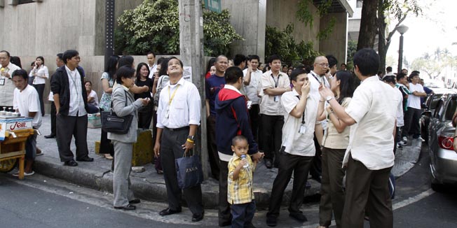 Employees gather on the side of a street after they rushed out of their office building after an earthquake Thursday, March 25, 2010 in Manila, Philippines. The 6.2 magnitude earthquake shook buildings and sent workers out of their offices in the city, though no immediate reports of damages or casualties. (AP Photo/Pat Roque)