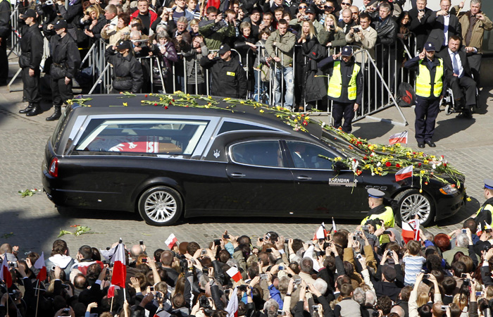 People stand along a street as a hearse carrying the coffin of the late Polish President Lech Kaczynski arrives in Krakaow, southern Poland, Sunday, April 18, 2010. The bodies of Kaczynski and his wife were flown from Warsaw to Krakow early Sunday for burial among Polish kings and poets at a tradition-laden ceremony that will be bereft of many world leaders whose travel plans were paralyzed by a plume of volcanic ash. (AP Photo/Markus Schreiber)