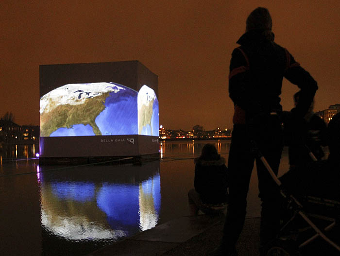 People watch an illuminated so-called CO2 cube is pictured in the water of St Jorgens Lake in front of Tycho Brahe Planetarium in Copenhagen, December 7, 2009. The cube visually shows the amount of carbon dioxide produced by an average person in one month.  REUTERS/Pawel Kopczynski (DENMARK)
