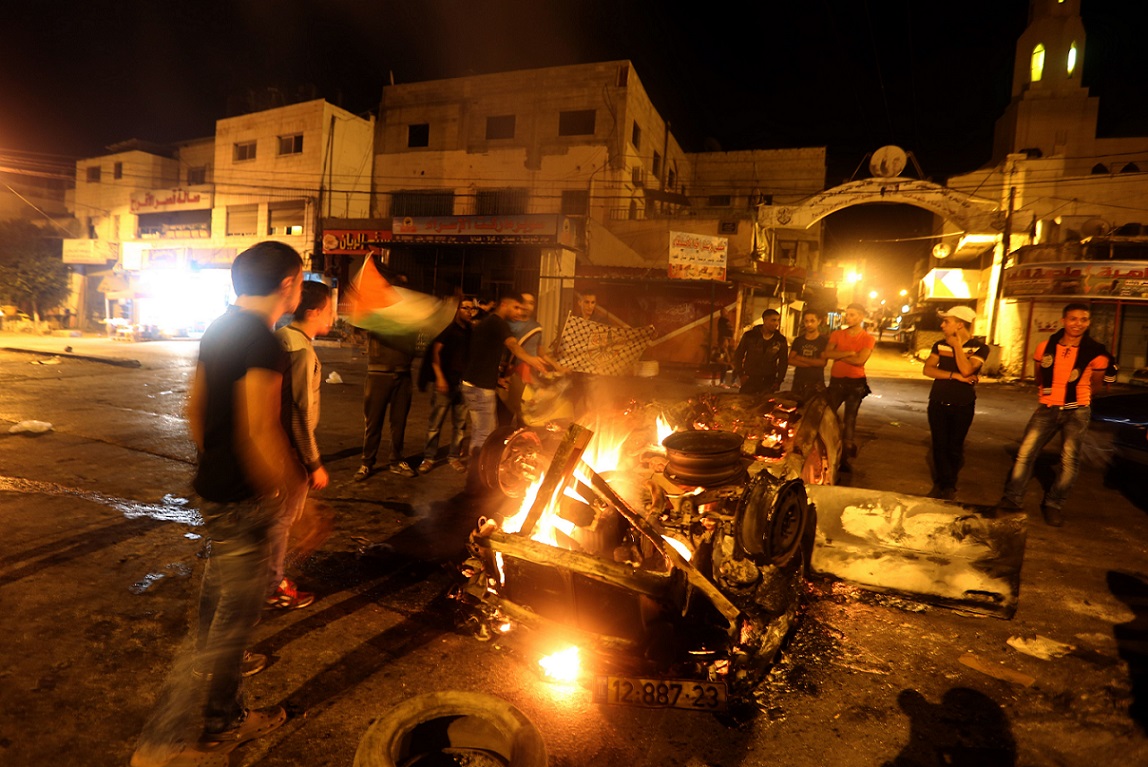 Palestinian youth stand next to a burning car belonging to an Israeli settler, that was set on fire by Palestinians as it entered the northern Palestinian West Bank city of Nablus, early on October 18, 2015, to visit and pray at Joseph's Tomb, a biblical figure from the book of Genesis, without the authorization of the Israeli army. The Israeli army arrested five settlers for entering the Palestinian territory without prior permission and escort, and evacuated the rest safely in coordination with Palestinian police in the area. AFP PHOTO/JAAFAR ASHTIYEH