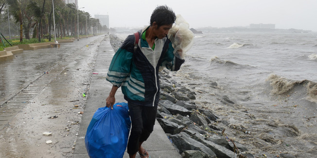 A man walks in the wind and rains brought on by typhoon Koppu along Roxas boulevard in Manila on October 18, 2015, as the typhoon hits Aurora province, northeast of Manila. Powerful Typhoon Koppu ripped off roofs, tore down trees and unleashed landslides and floods, forcing thousands to flee as it pummelled the northern Philippines on October 18, officials said.   AFP PHOTO / TED ALJIBE