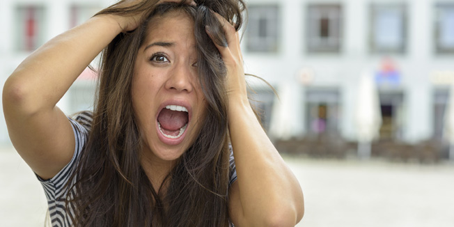 Woman yelling in horror and fear while tearing at her hair with a look of panic outdoors on an urban street, close up of her face