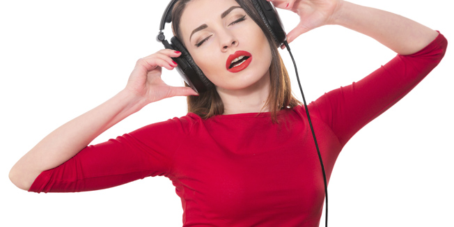 Pretty girl listening to the music with closed eyes touching big headphones isolated on white background