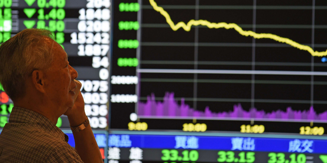 A man speaks in front of monitors showing market movements at the Taiwan Stock Exchange in Taipei on July 8, 2015.  Taiwan's weighted index fell 274.05 points or 2.96 percent to 8,976.11 as a rout in China spread into regional markets while traders are also buffeted by fears about Greece's future in the eurozone.  AFP PHOTO / Sam Yeh