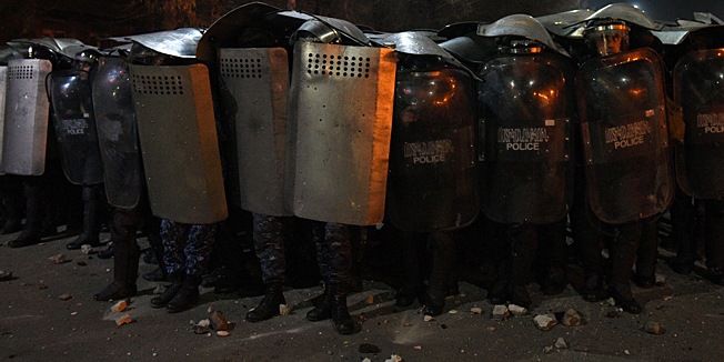 Armenian police officers hold up their shields as they stand guard during clashes with protesters at a demonstration near the Russian Consulate General in Gyumri, north-western Armenia, on January 15, 2015, to demand that Russian soldier Valery Permyakov accused of murdering a family of six be delivered to Armenian justice authorities for trial. Permyakov allegedly gunned down the family members in a bloody shooting spree on January 12 before disappearing from a Russian military base where he was stationed in Gyumri before being arrested. AFP PHOTO / KAREN MINASYAN