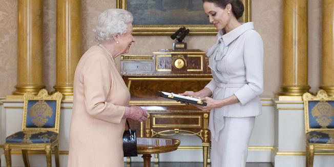 US actress Angelina Jolie (R) is presented with the Insignia of an Honorary Dame Grand Cross of the Most Distinguished Order of St Michael and St George by Britain's Queen Elizabeth II in the 1844 Room at Buckingham Palace in central London, on October 10, 2014. Angelina Jolie was awarded an honorary damehood (DCMG) for services to UK foreign policy and the campaign to end war zone sexual violence. AFP PHOTO/Anthony Devlin/POOL