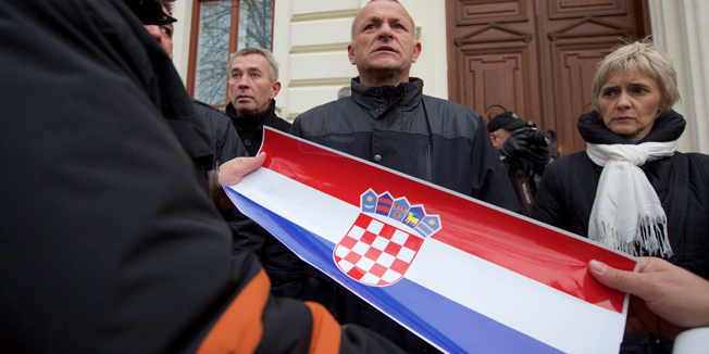 Vukovar, 031214.Jutros u 9. sati na Opcinskom sudu u Vukovaru nastavljeno je sudjenje hrvatskim braniteljima koji su prosle godine razbijali dvojezicne ploce na drzavnim zgradama.Za vrijeme sudjenja clanovi Stozera za obranu hrvatskog Vukovara krenuli su s akcijom lijepljenja hrvatskih zastava preko dvojezicnih natpisa,zastavicama su prekrili cirilicni natpis ustanove.Na fotografiji: lijepljenje hrvatske zastavice preko cirilcnog natpisa na dvojezicnim plocama,zgrada Drzavne uprave.Foto: Vlado Kos / Cropix