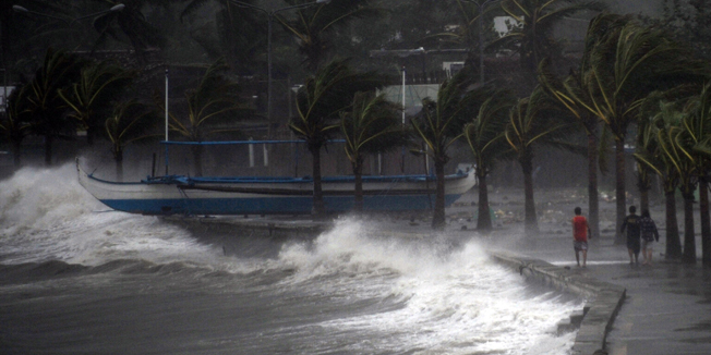 Residents walk past high waves brought about by strong winds as it pound the seawall, hours before Typhoon Hagupit passes near the city of Legazpi on December 7, 2014.  Typhoon Hagupit tore apart homes and sent waves crashing through coastal communities across the eastern Philippines, creating more misery for millions following a barrage of deadly disasters.      AFP PHOTO/TED ALJIBE