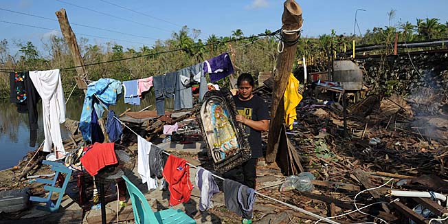 A resident carries a religious icon, one of her belongings saved from their house destroyed at the height of Typhoon Hagupit at a village along a highway in Sulat town, Eastern Samar province, on December 9, 2014.  Hagupit, the strongest storm to hit the disaster-ravaged country this year has claimed at least 23 lives since smashing into the archipelago, bringing winds of 210 kilometres (130 miles) an hour. AFP PHOTO / TED ALJIBE