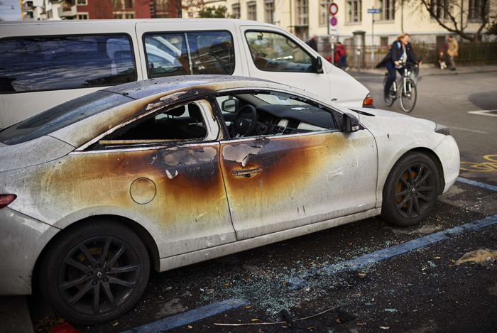 A woman rides her bicycle past a burnt car after a night of riots in Zurich on December 13, 2014. Police fired tear gas and water cannon in central Zurich to disperse some 200 masked radicals who attacked officers and set cars, trees and trash bins on fire, sending terrified residents fleeing in the upscale and normally tranquil neighbourhood. AFP PHOTO/MICHAEL BUHOLZER