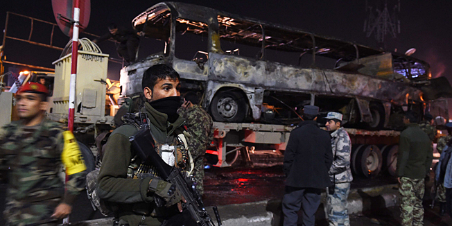 An Afghan soldier wields his weapon as he stands next to the burned out wreckage of an army bus at the scene of a suicide attack in Kabul on December 13, 2014. A suicide attack targeting an Afghan army bus killed at least six soldiers in Kabul on December 13, officials said, adding that the death toll could rise. AFP PHOTO/ROBERTO SCHMIDT