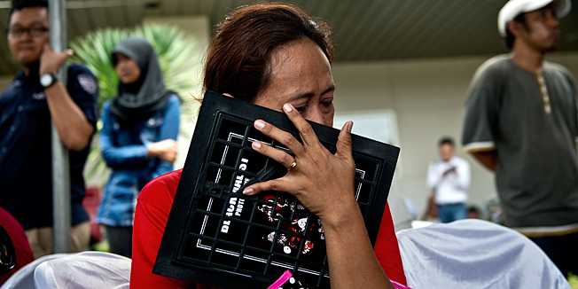 An Indonesian woman breaks down while holding a family picture of passengers onboard the missing Malaysian air carrier AirAsia flight QZ8501, outside the crisis-centre set up at Juanda International Airport in Surabaya on December 29, 2014. The AirAsia plane which went missing with 162 people on board en route for Singapore is likely at the bottom of the sea, Indonesia's National Search and Rescue Agency chief said on December 29.   AFP PHOTO / MANAN VATSYAYANA
