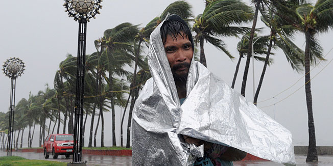 A man walks through heavy wind and rain as Typhoon Rammasun barrels across Manila on July 16, 2014. Typhoon Rammasun shut down the Philippine capital on July 16 as authorities said the first major storm of the country's brutal rainy season claimed at least one life and forced hundreds of thousands to evacuate.  AFP PHOTO / Jay DIRECTO