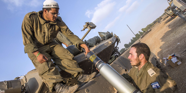 Israeli soldiers carry a shell as they prepare their Merkava tanks stationed at an army deployment along the Israeli Gaza border, on July 22, 2014.  AFP PHOTO / JACK GUEZ
