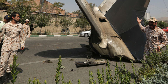 A member of the Iranian Revolutionary Guards reacts as he stands next to the remains of a plane that crashed near Tehran's Mehrabad airport on August 10, 2014. A civilian airliner crashed on take-off near the Mehrabad airport in the capital, Iranian news agencies said, with reports that almost 50 people were killed. AFP PHOTO / ATTA KENARE