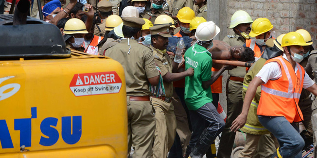 Indian rescue workers carry a survivor (C) pulled from the wreckage of a collapsed apartment building in Chennai on June 30, 2014. Rescuers plucked two survivors from the ruins of a collapsed apartment block in southern India as they raced against the clock to find dozens more people feared trapped in the rubble. The confirmed death toll from the disaster on the outskirts of Chennai rose to 18 as authorities blamed shoddy construction for what was the second deadly building collapse in India within a matter of hours. Reports said that the two people rescued morning included a 35-year-old female construction worker who was one of several dozen entombed by a mass of concrete.