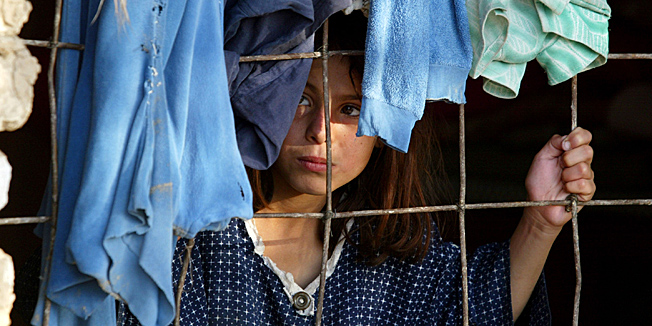 BAGHDAD, IRAQ - OCTOBER 17:  An Iraqi girls looks out from her bedroom window at the Al Rashid military base where 2000 families live October 17, 2003 in Baghdad, Iraq. Financially displaced Iraqi's took over the military base after it was bombed by the U.S. forces during the war and was left in ruins, abandoned by the Iraqi Army. They have no running water, are unemployed and have been forced to seek free housing.  (Photo by Paula Bronstein/Getty Images) 