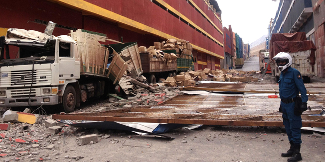 Picture of a lorries destroyed by parts of a building damaged by a quake and its aftershocks, in Iquique 1,950 km north of Santiago on April 3, 2014. Chileans desperate for supplies stood in long lines outside shops on Thursday after strong aftershocks from a deadly 8.2-magnitude earthquake forced them to spend another night out in the cold. After six people were killed in late Tuesday's earthquake, northern Chile was rocked by a powerful 7.6-magnitude aftershock Wednesday night, forcing thousands of people to evacuate their homes once more.    AFP PHOTO/ALDO SOLIMANO