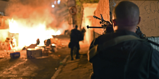 A Brazilian Police Special Force member takes position during a violent protest in Copacabana, Rio de Janeiro on April 22, 2014. People took to the streets and burnt tyres during a protest following the death of a young dancer last weekend in a nearby favela, during clashes with the Army.   AFP PHOTO / CHRISTOPHE SIMON