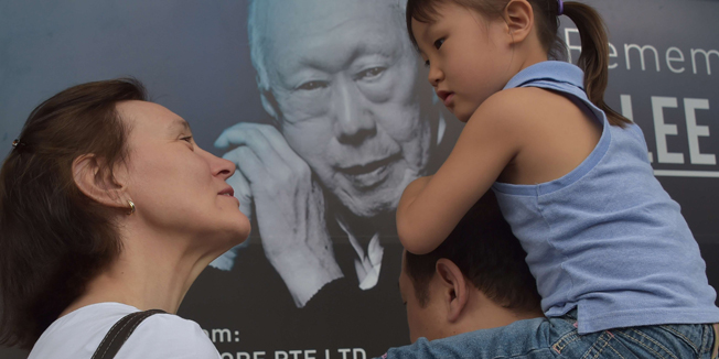 A family is seen in front of a memorial portrait of Singapore's late former prime minister Lee Kuan Yew outside the parliament building where he lies in state ahead of his funeral in Singapore on March 28, 2015. Singapore's first prime minister Lee Kuan Yew, one of the towering figures of post-colonial Asian politics, died at the age of 91 on March 23. AFP PHOTO / ADEK BERRY 