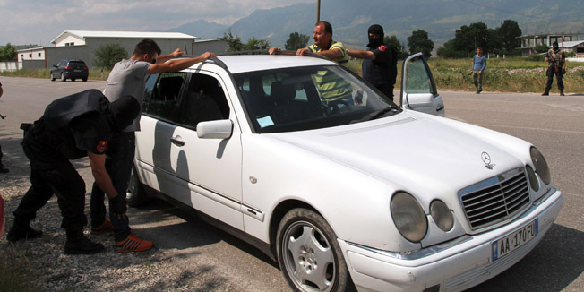 Albanian police officers pat down two men as they perform checks on cars in the village of Lazarat, south of the Albanian capital Tirana, on June 16, 2014. Suspected drug traffickers fired heavy machine guns and rocket propelled grenades on June 16 at Albanian police attempting to enter a village renowned for its mass cannabis production, authorities said. Police said at least 500 officers tried to access Lazarat, 240 kilometres (150 miles) south of Tirana, in order to destroy the village's drug stockpile. The force came under heavy arms fire, including anti-tank rockets, it said. According to Italian police the village produces 900 tonnes of cannabis each year worth some 4.5 billion euros ($6.1 billion) -- equivalent to almost half of Albania's gross domestic product. AFP PHOTO / GENT SHKULLAKU