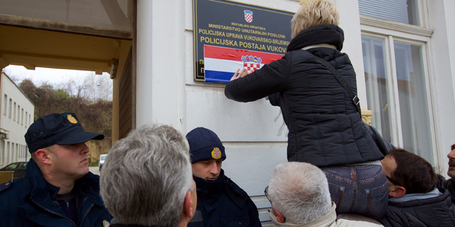 Vukovar, 031214.Jutros u 9. sati na Opcinskom sudu u Vukovaru nastavljeno je sudjenje hrvatskim braniteljima koji su prosle godine razbijali dvojezicne ploce na drzavnim zgradama.Za vrijeme sudjenja clanovi Stozera za obranu hrvatskog Vukovara krenuli su s akcijom lijepljenja hrvatskih zastava preko dvojezicnih natpisa,zastavicama su prekrili cirilicni natpis ustanove.Na fotografiji: lijepljenje hrvatske zastavice preko cirilcnog natpisa na dvojezicnim plocama na zgradi Policijske postaje u Vukovaru.Foto: Vlado Kos / Cropix
