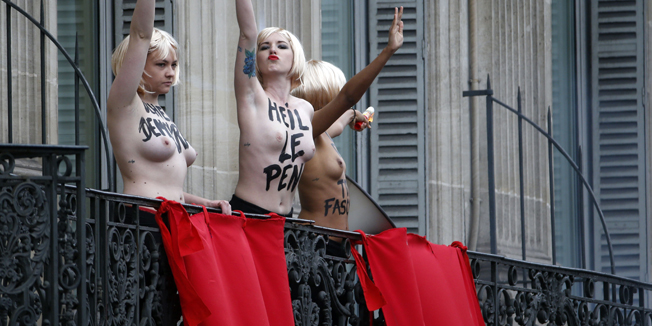 Femen activists demonstrate on a balcony during a rally called by France's far-right political party Front National (FN) Marine Le Pen during the party's annual rally in honour of Jeanne d'Arc (Joan of Arc) on May 1, 2015 in Paris.    AFP PHOTO / KENZO TRIBOUILLARD