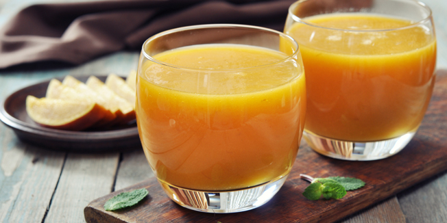Mango smoothie in glass with mint on wooden background