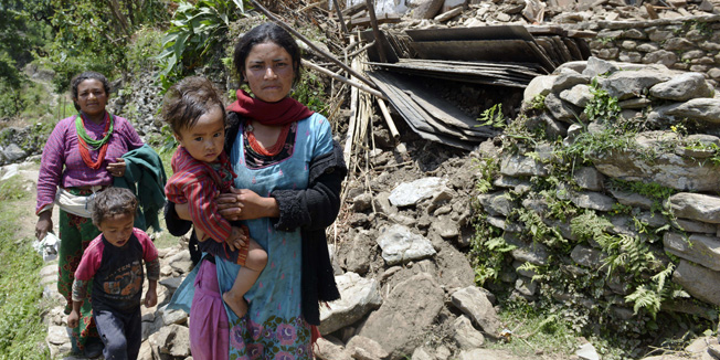 Two women walk past the remains of a collapsed house on this village in northeastern Nepal on their way to see a team of doctors from Medecins Sans Frontiers (MSF) who had flown in on a helicopter on May 14, 2015 to assist victims of the latest earthquake. Two strong earthquakes struck Nepal killing over 8,000 people and leaving hundreds of thousands homeless within a period of three weeks.  AFP PHOTO / PRAKASH MATHEMA