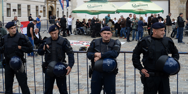Zagreb, 280515.Markov trg.Nakon sto su se pridruzili prosvjedu Imunoloskog zavoda, branitelji prosvjednici danas su predvodjeni Djurom Glogoskim dosli na Markov trg trazeci sastanak sa premijerom. Na trg su donijeli i suncobrane te se sklonili pod njima.Na fotografiji: policijsko osiguranje i branitelji prosvjednici.Foto: Goran Mehkek / CROPIX